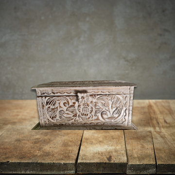 Decorative wooden box with floral carvings on a wooden surface with a gray background