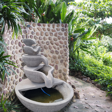 Outdoor water fountain with a pebble wall and greenery