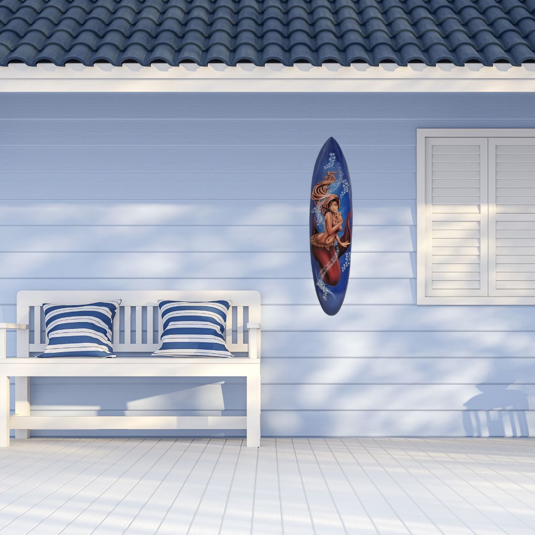 Surfboard with a design of a woman on a wall next to a white bench with striped cushions.
