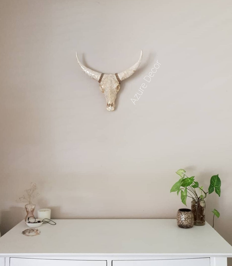Decorative bull skull on a plain wall above a white surface with plants and vases.