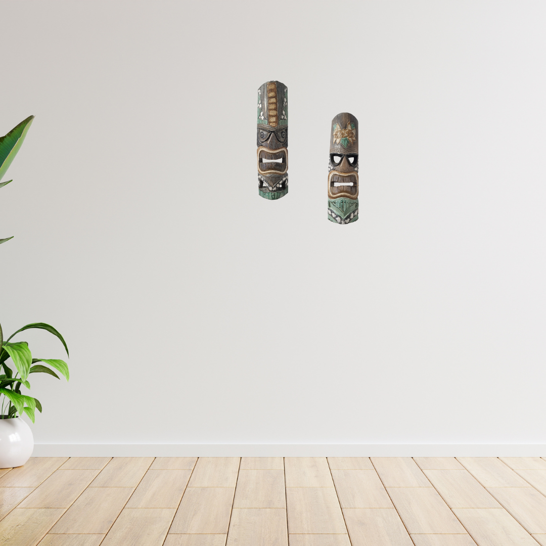 Two decorative masks on a white wall with a plant on a wooden floor.