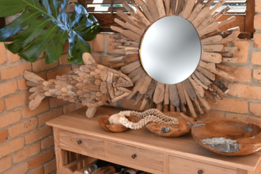 Wooden fish sculpture, sunburst mirror, and decorative bowls on a wooden console against a brick wall.