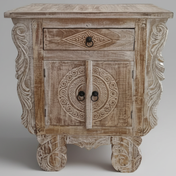 Close-up front view of a Balinese carved reclaimed teak bedside table showing circular medallion cabinet doors with ring pulls, diamond-carved drawer, and ornate scrollwork side panels in chalky whitewash finish