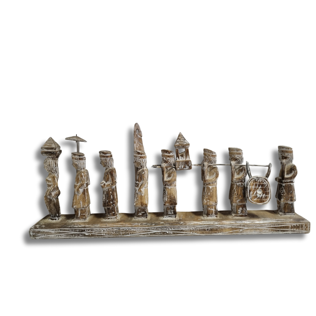 A handcrafted Balinese wooden statue depicting multiple figures in traditional attire, carved in a rustic style with a neutral color palette.