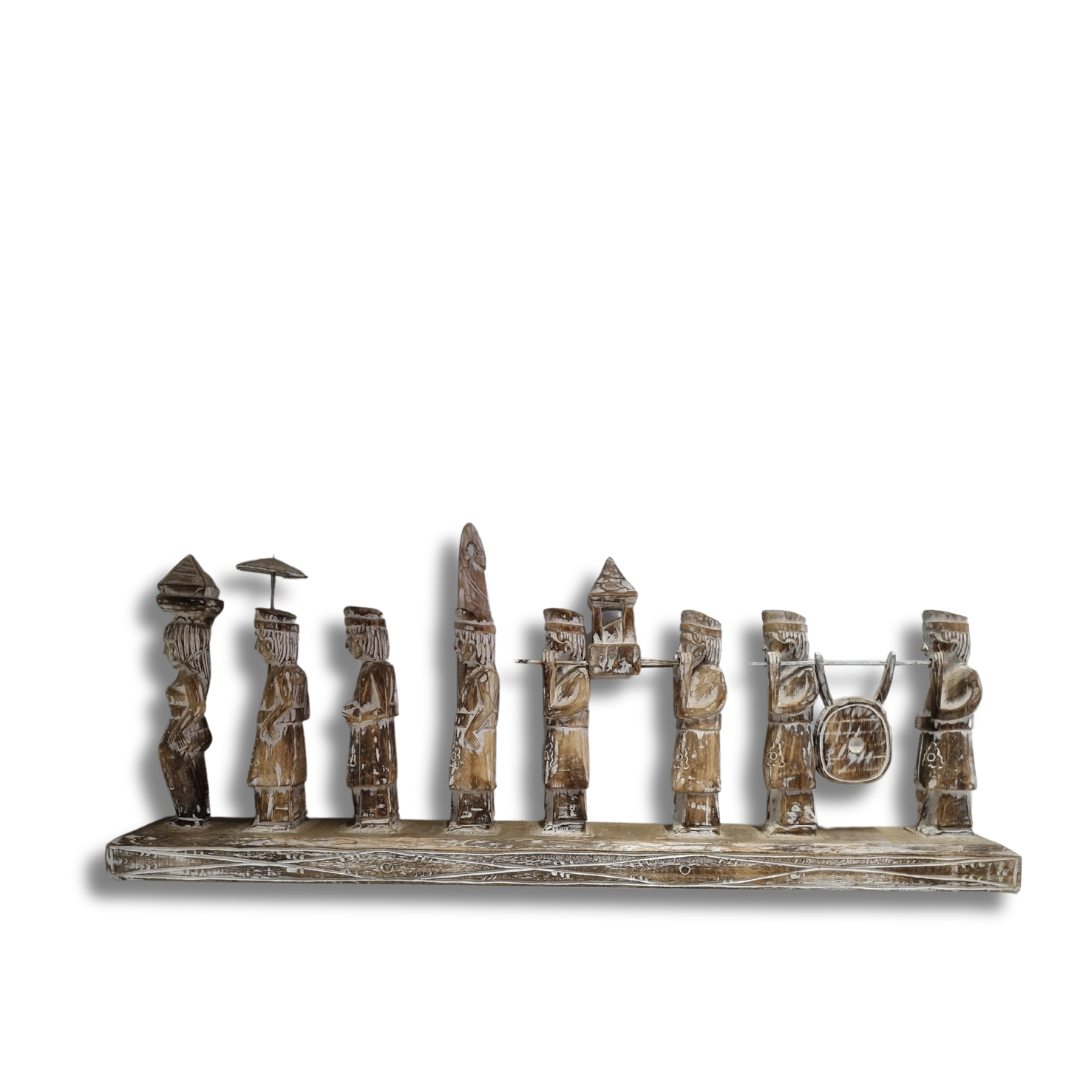 A handcrafted Balinese wooden statue depicting multiple figures in traditional attire, carved in a rustic style with a neutral color palette.