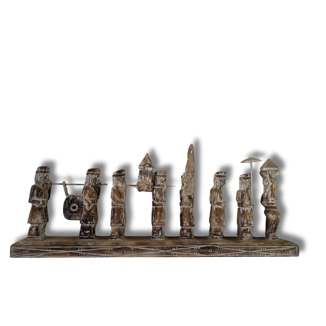 A handcrafted Balinese wooden statue depicting multiple figures in traditional attire, carved in a rustic style with a neutral color palette.