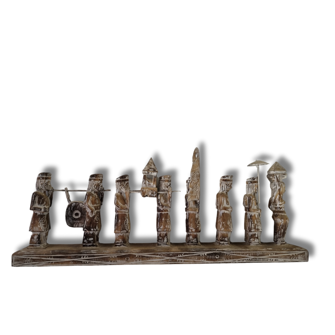 A handcrafted Balinese wooden statue depicting multiple figures in traditional attire, carved in a rustic style with a neutral color palette.