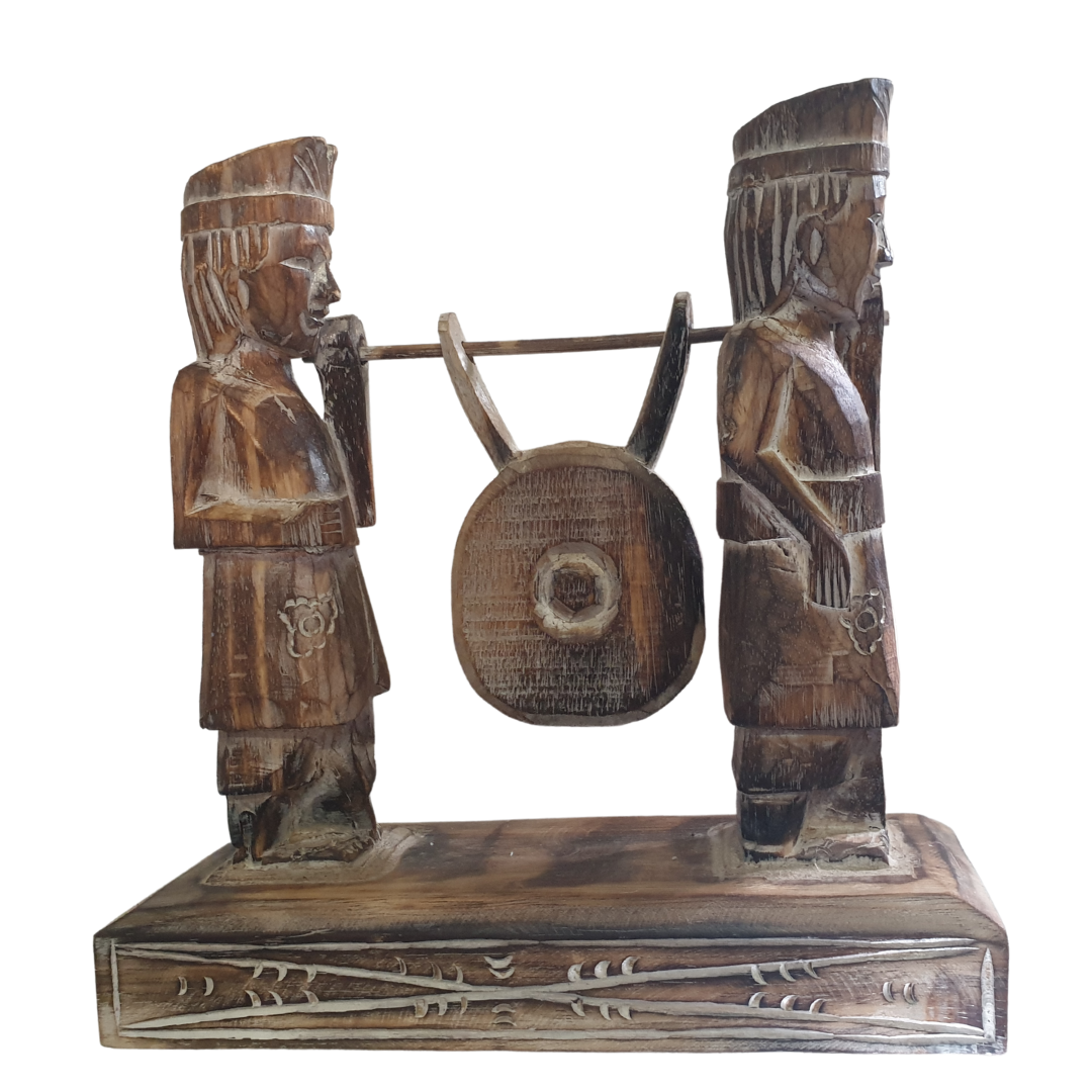 A wooden statue depicting two Balinese figures in traditional ceremony attire, standing on a platform.