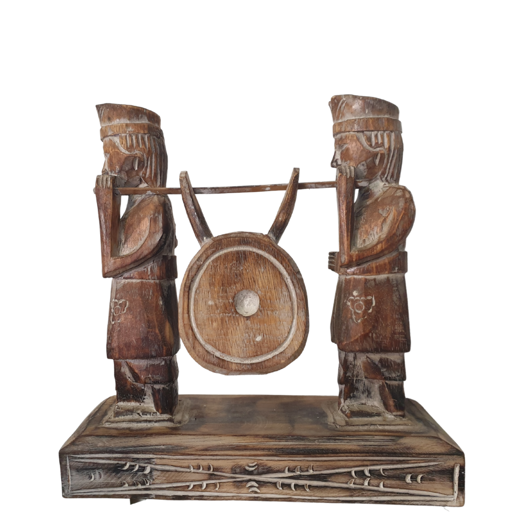 A wooden statue depicting two Balinese figures in traditional ceremony attire, standing on a platform.