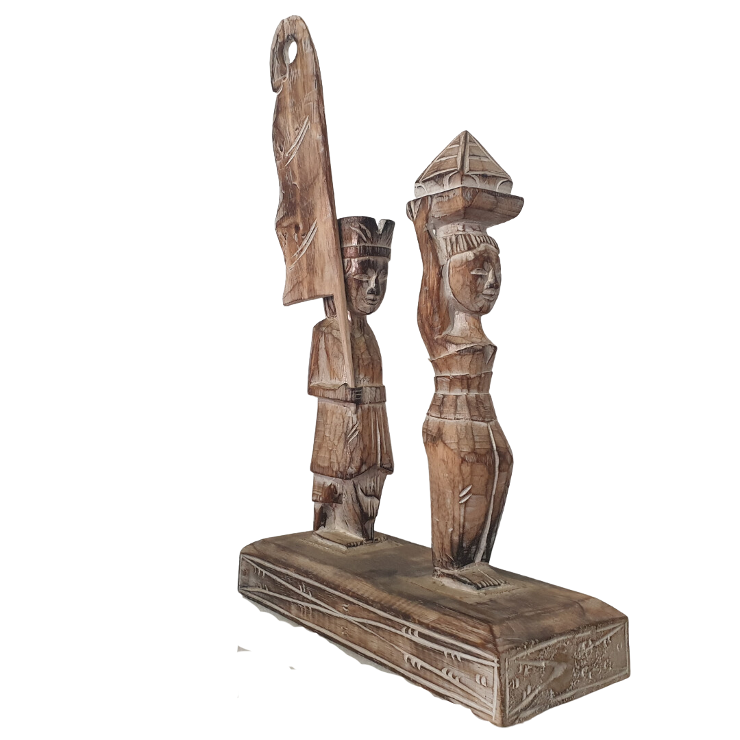 A wooden statue depicting two Balinese figures in traditional ceremony attire, standing on a platform.