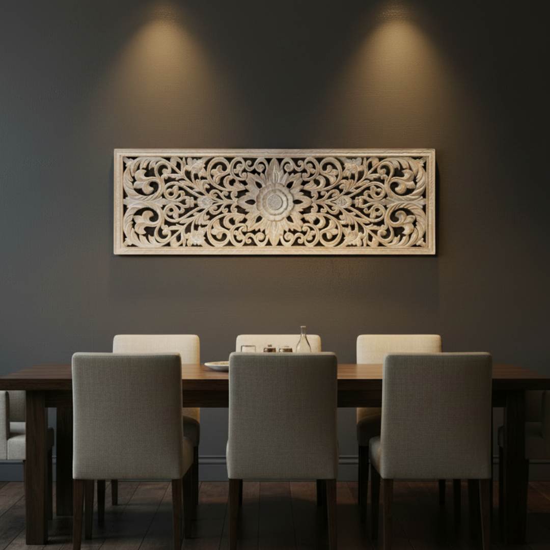 Whitewash precision-cut MDF wall art panel with Balinese floral scroll design hung on a dark charcoal feature wall above a long dark dining table with cream upholstered chairs, dramatically lit by three ceiling spotlights