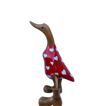 Side view of a glossy scarlet body with white hearts, a curved natural timber neck and brown boots, facing right