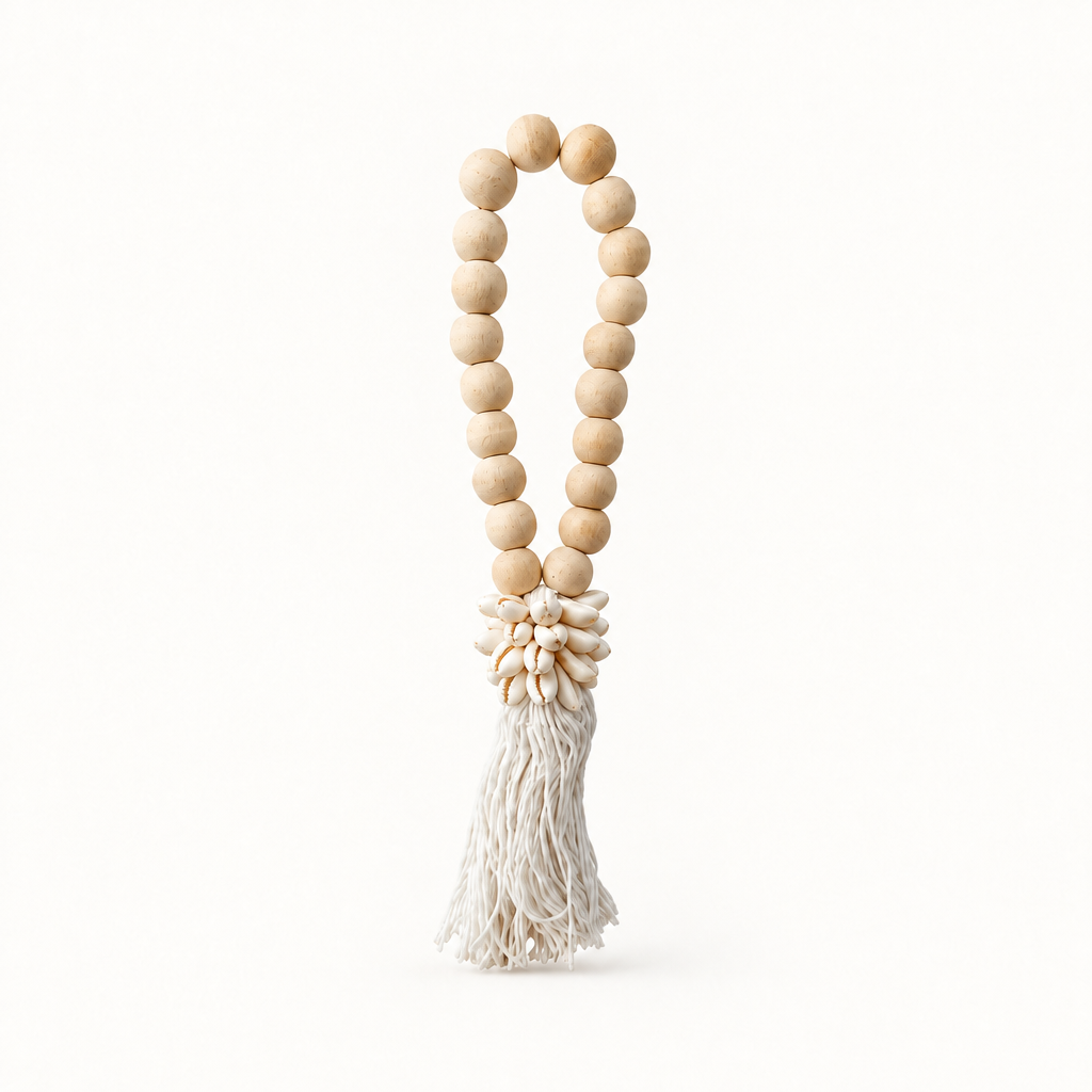 White cotton strands beneath a cowrie cluster and an oval loop of natural wooden beads on a plain background