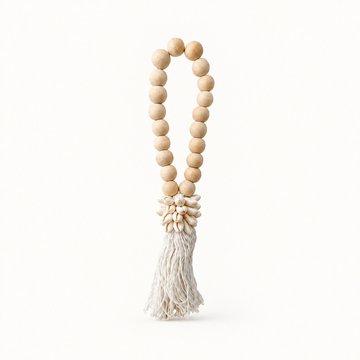 White cotton strands beneath a cowrie cluster and an oval loop of natural wooden beads on a plain background