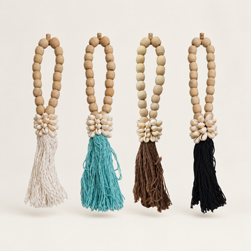 Four colour options in white, turquoise, brown and black, each with a wooden bead loop and cowrie detail against a cream background.