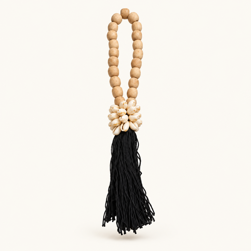 Black cotton strands below an oval wooden loop and a cluster of cowrie shells