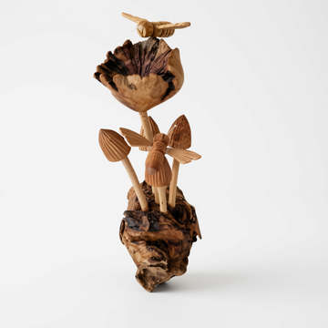 Tall sculptural cluster of carved mushrooms and bees rising from a rough textured root base, light grey background.