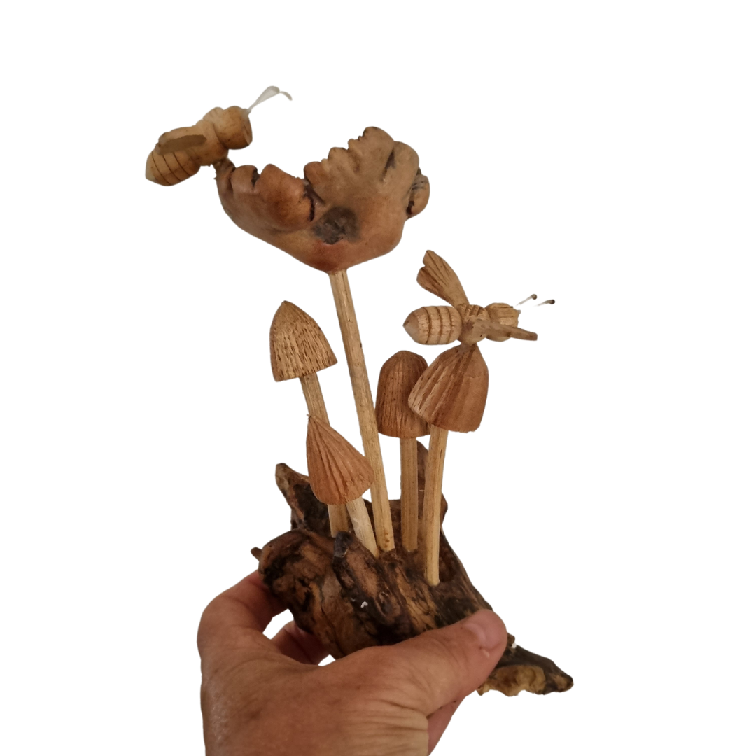Figurine of fungi and insects on a root base, held in a person's hand against a white background
