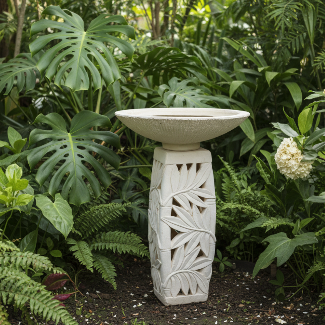 Concrete pedestal with carved tropical leaf detail in a garden setting, lush green foliage, natural white finish