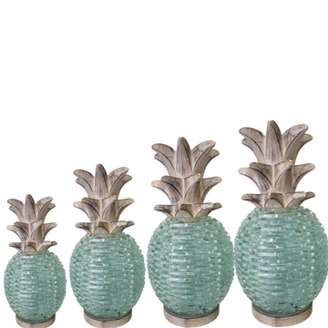 Four sizes of Boho Glass Pineapple Décor displayed together — small, medium, large and extra large — featuring aqua sea-glass textured bodies with whitewashed carved wooden leaf tops, handcrafted tropical boho tabletop sculpture by Azure Decor