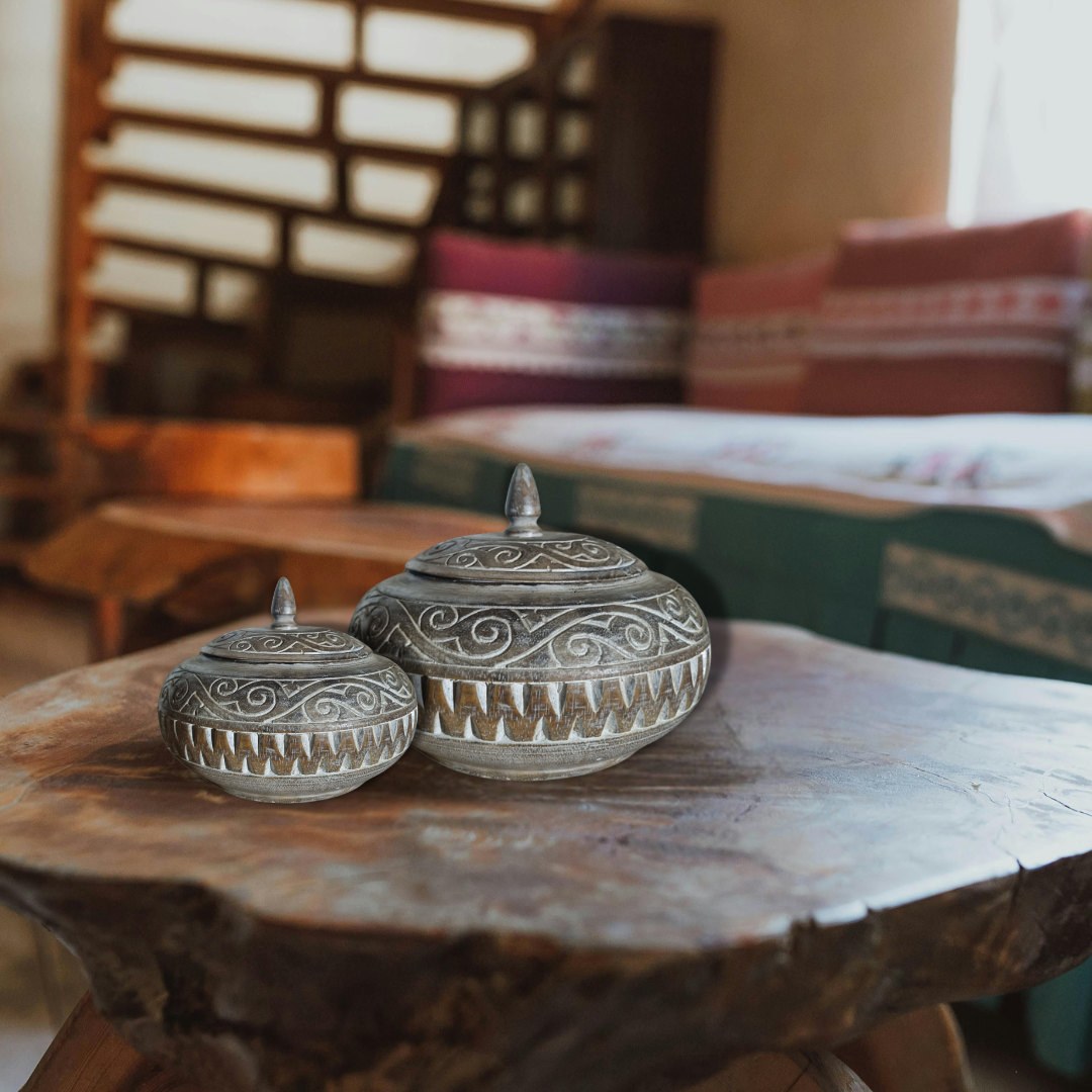 Two decorative stone jars on a wooden table with a blurred indoor setting in the background.