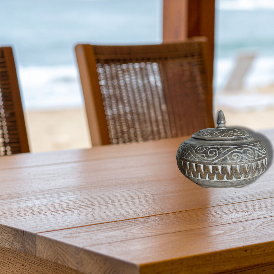 Decorative metal container on a wooden table with blurred chairs and background