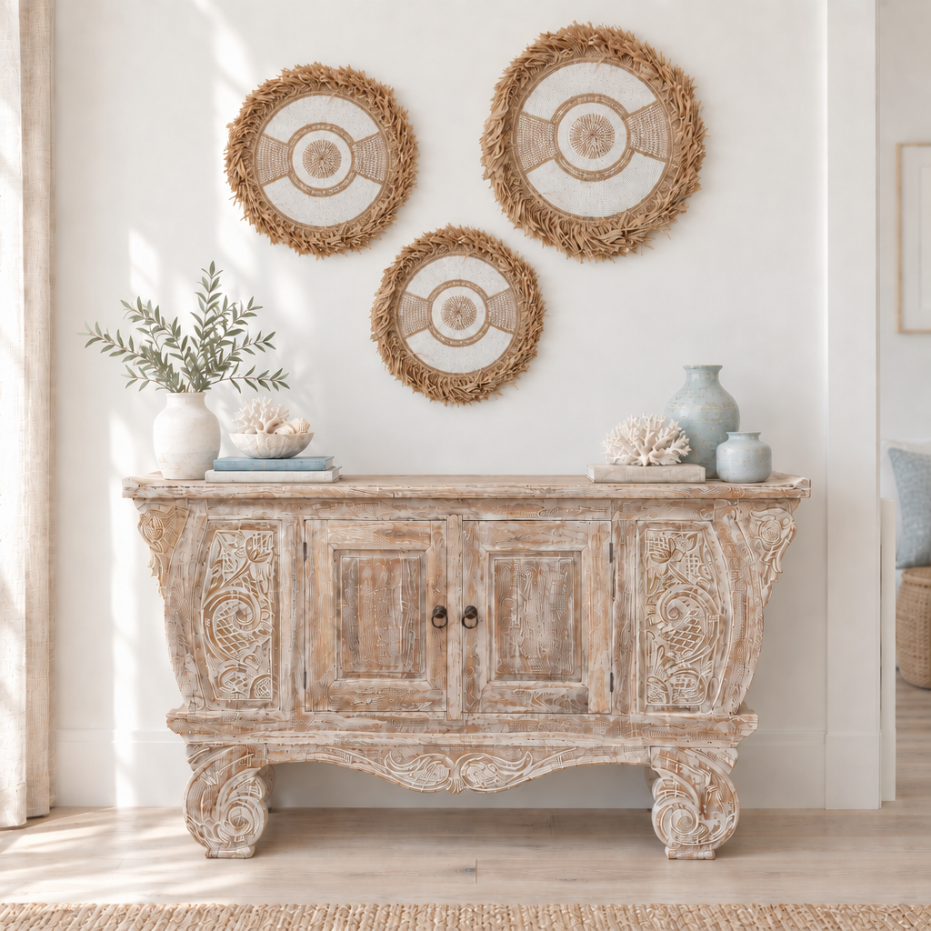Three natural shell-and-bead pieces with raffia fringe arranged above a weathered carved timber cabinet