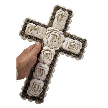 Hand holding a white and brown decorative piece to show its size and raised floral detailing