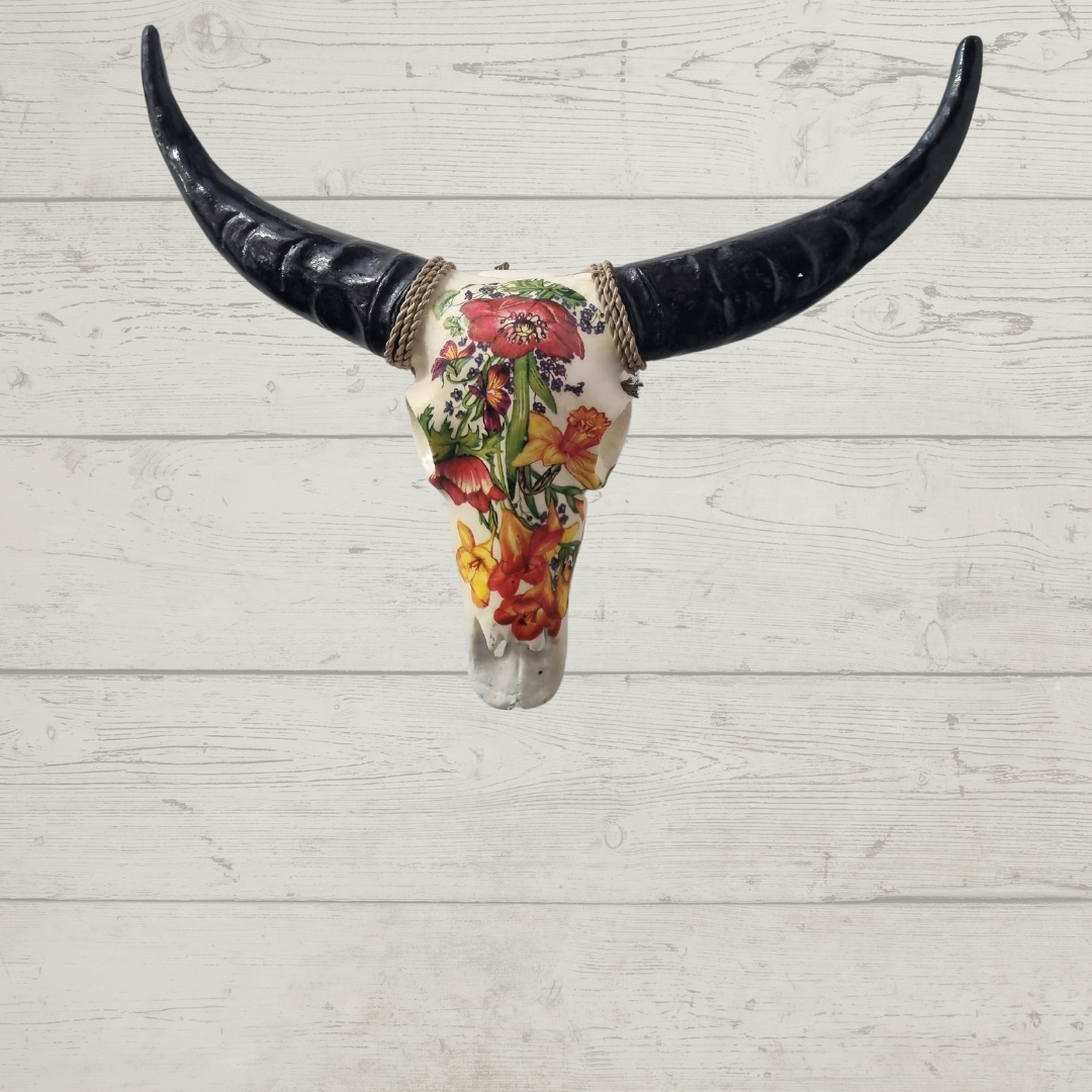 Floral resin bull skull wall decor with vibrant red, orange and yellow poppy and freesia design and black horns with jute rope, mounted against whitewashed timber wall — boho farmhouse wall art