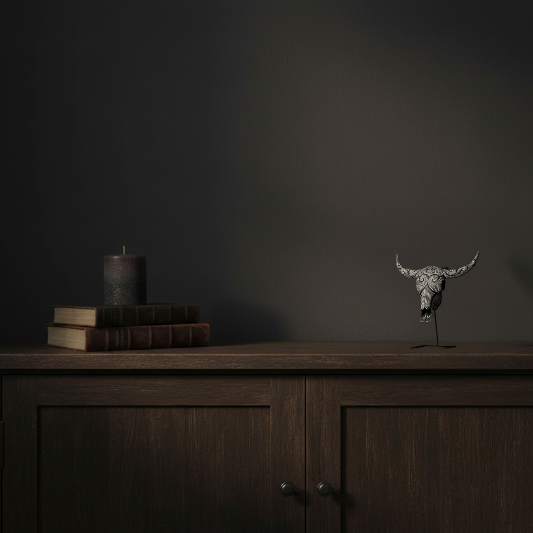 Night Bull Skull – hand-painted black and white dot mandala bull skull on black metal stand displayed on a dark wooden cabinet in a moody dramatic interior with candle and ambient lighting
