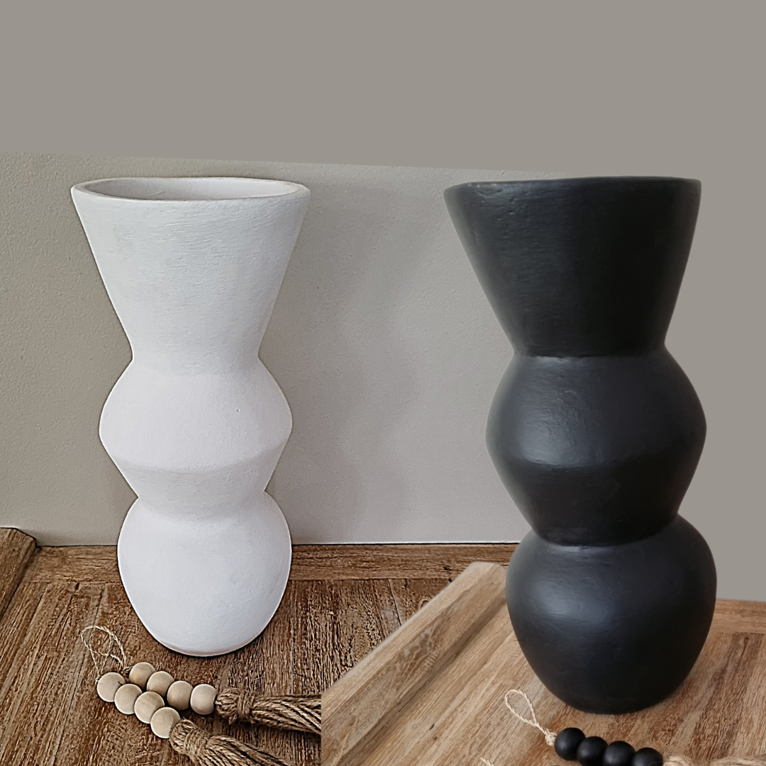 Two vases, one white and one black, on a wooden surface with a neutral background.