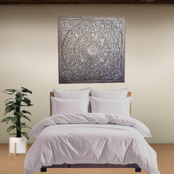 Neatly made bed with gray bedding in a room with a decorative wall art piece.