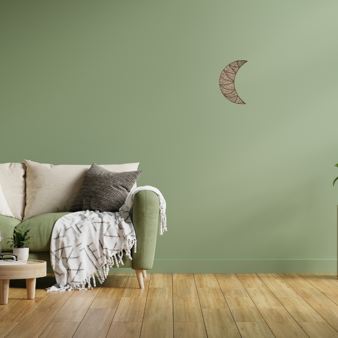 Sofa with decorative pillows and a blanket against a green wall with a moon-shaped wall art piece.