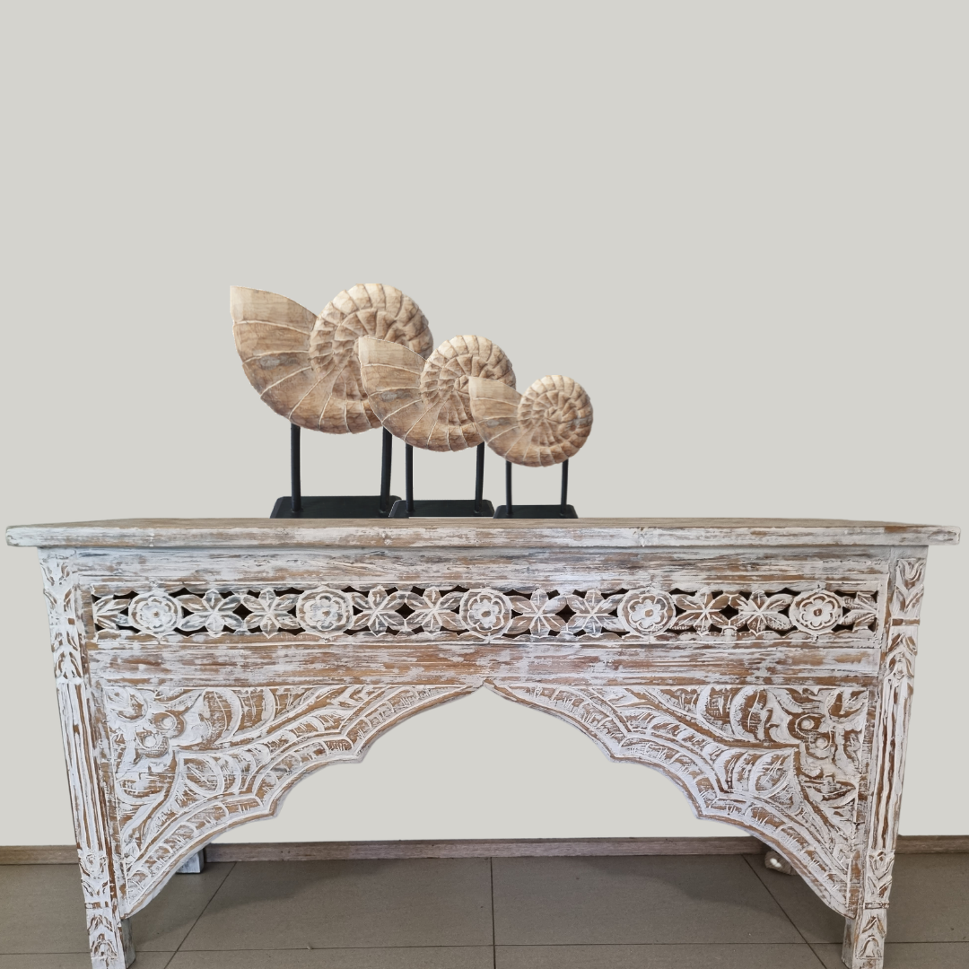 Decorative wooden console table with intricate carvings and three large seashells on a plain background