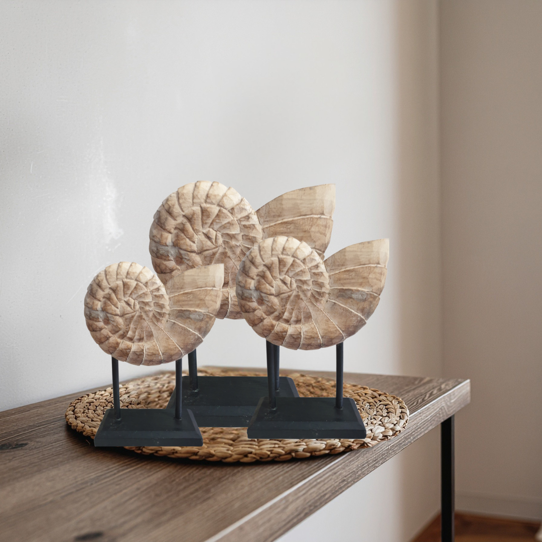 Set of three hand-carved wooden nautilus shell sculptures on black metal stands styled on a timber console table with woven rattan placemat – coastal Hamptons home decor by Azure Decor