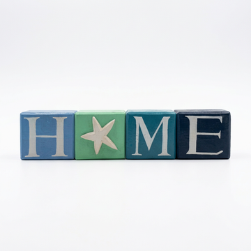 White background, blocks together
“Coastal HOME wooden blocks in blue, green, teal and navy, with cream lettering and a starfish replacing the O