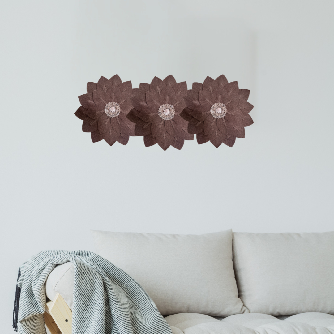 Three brown flower-shaped wall decorations on a white wall above a beige sofa.