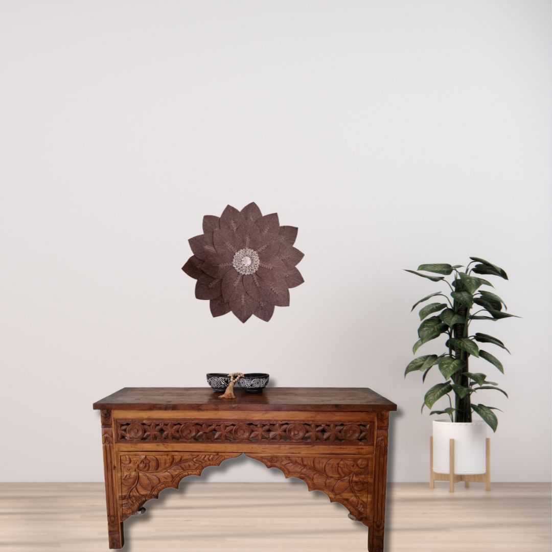 Macramé decorative wall art in brown and beige tones displayed above a wooden console table with a plant against a light background.