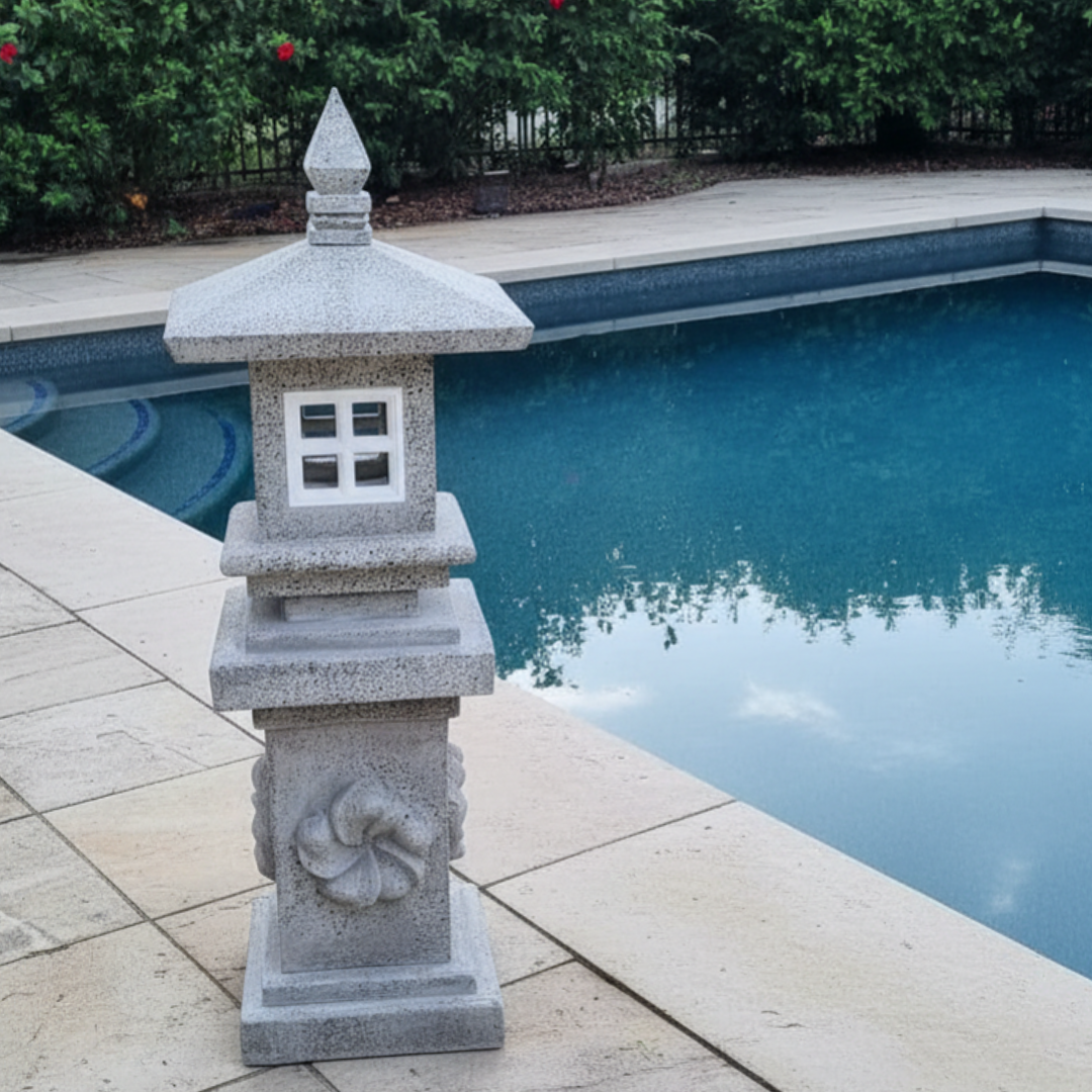 Tiered stone sculpture with carved spiral column and square window opening positioned on travertine pool coping beside a blue swimming pool with lush green hedging