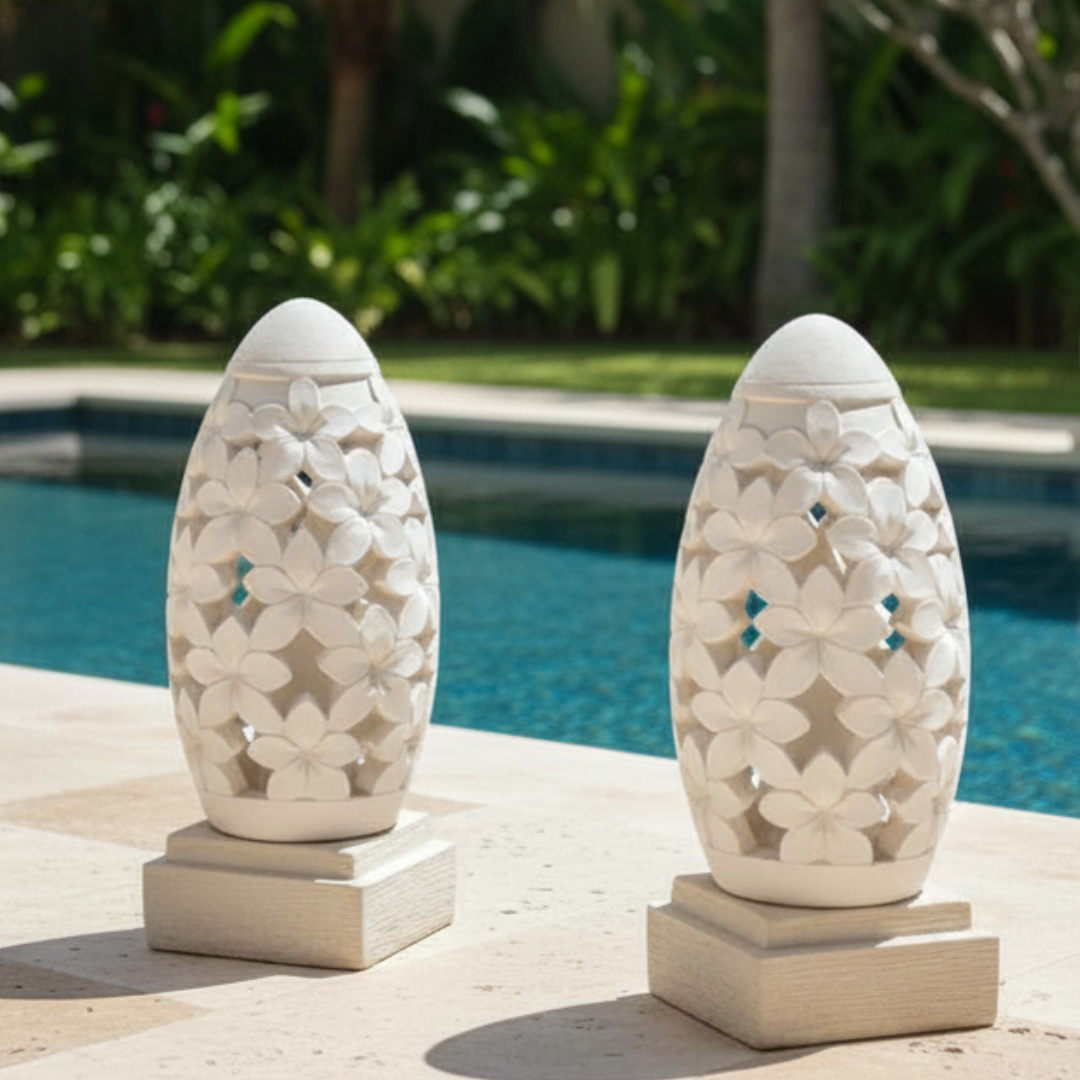Two decorative stone lanterns by a pool with greenery in the background