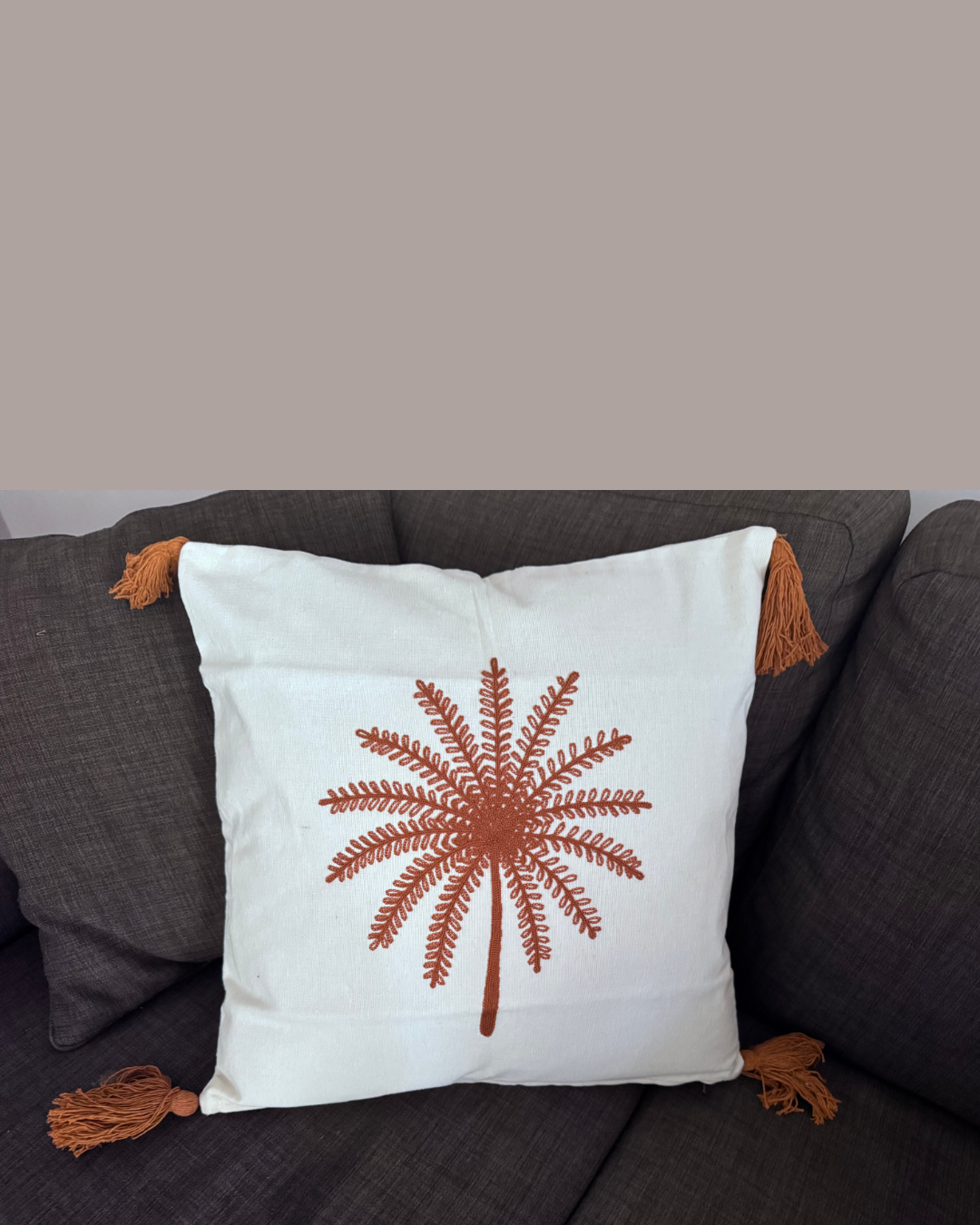 Decorative pillow with a palm tree design on a gray sofa.
