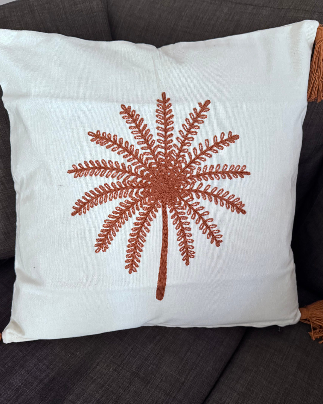 White pillow with brown embroidered palm tree design on a dark surface