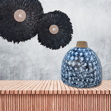 Decorative black feathered wall hangings above a textured blue vase on a wooden surface.