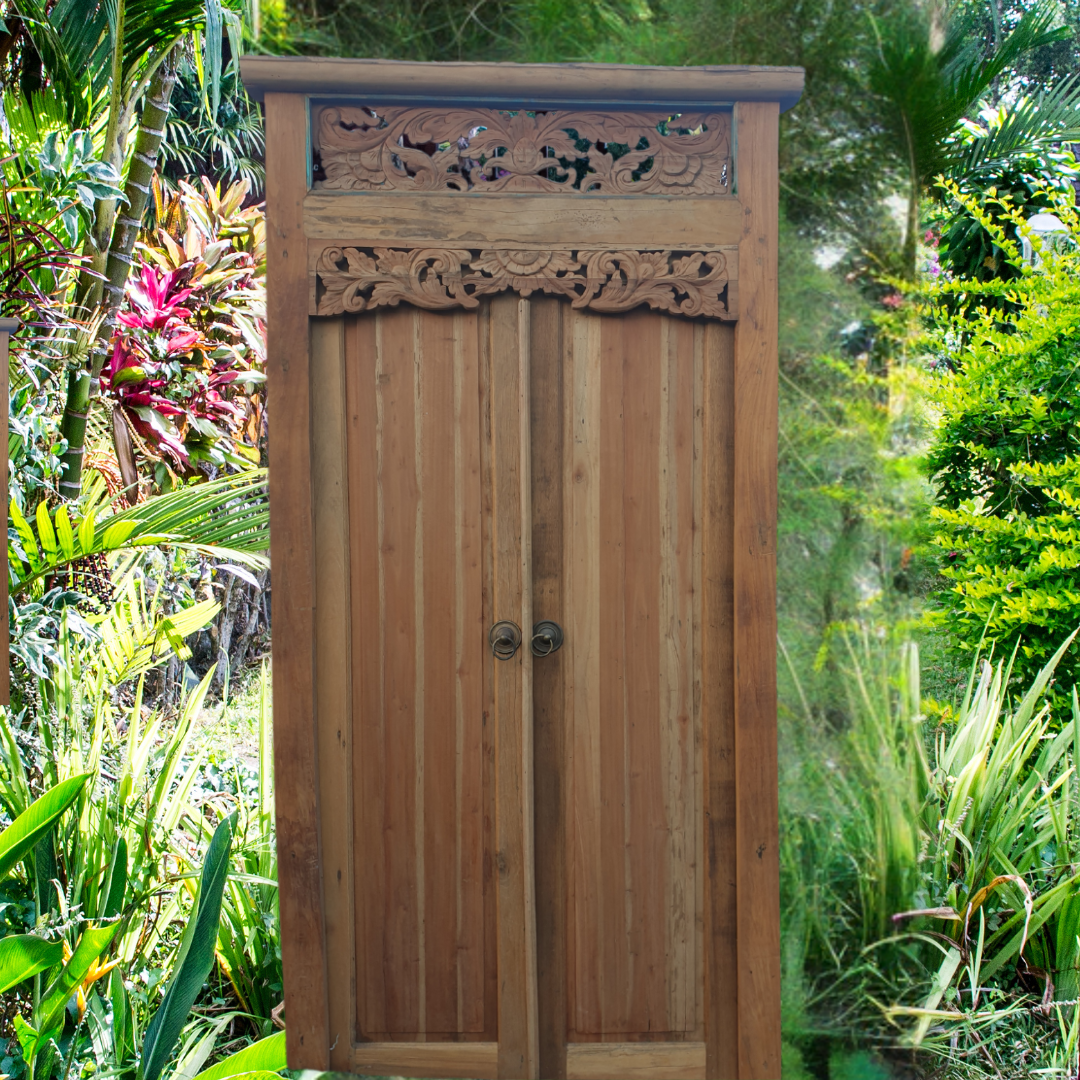 Wooden Balinese style door with intricate carvings in a lush green garden setting