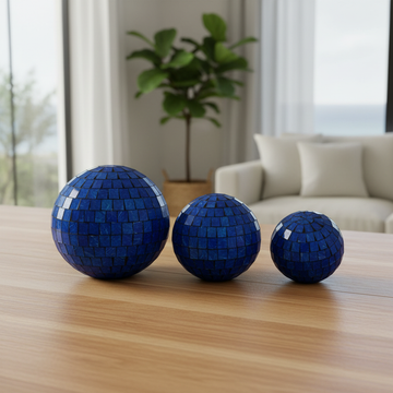Three blue glass mosaic spheres arranged on a warm timber tabletop in a bright living room