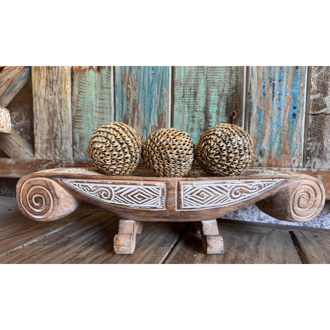 Wooden bowl with decorative patterns holding three woven balls against a rustic wooden background.