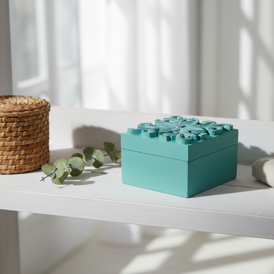 Square teal decorative on a white table top cane and leafy greens 