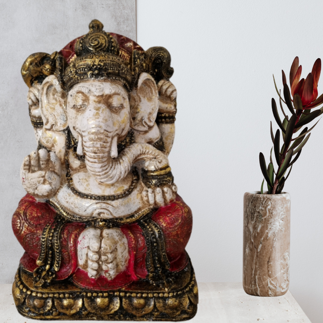 Decorative statue of a seated figure with intricate details next to a vase with red flowers on a light surface.
