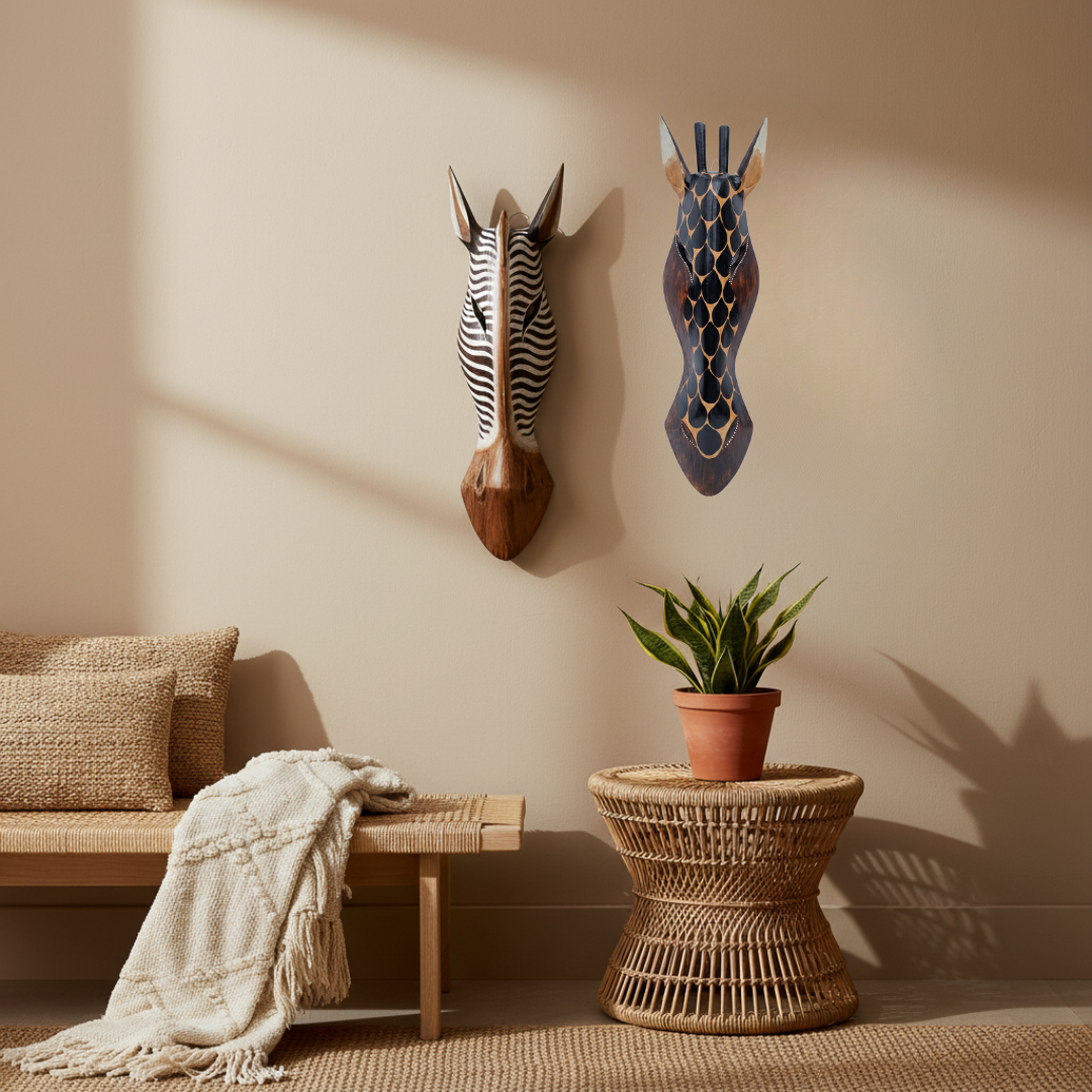 Two decorative animal head wall sculptures displayed on a beige wall in a styled room setting, with a woven bench, throw blanket, potted plant, and wicker side table below.