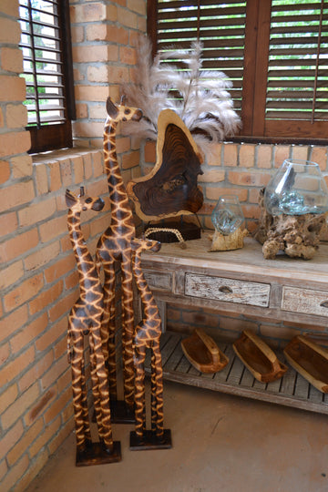 Home decor pieces set in a rustic brick back ground 3 wooden giraffes set next to a wooden console table with additional decor items to completment a coastal or rustic vibe